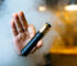 Person, der holder en sort e-cigaret i hånden med damp i baggrunden